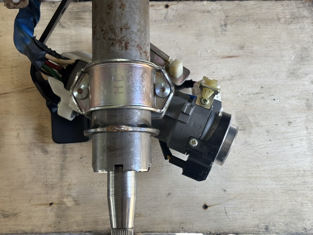 Factory steering column ignition lock housing with tamper-proof security bolts installed on metal clamp.